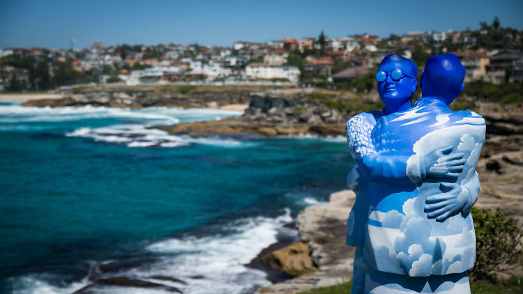 A sculpture of two people with their bodies painted like the sky embracing Sculpture by the Sea 2017