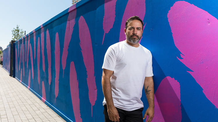 Reko Rennie stands in front of his art work As The Crow Flies