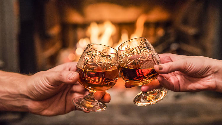 Hands toasting with whiskey in front of fireplace