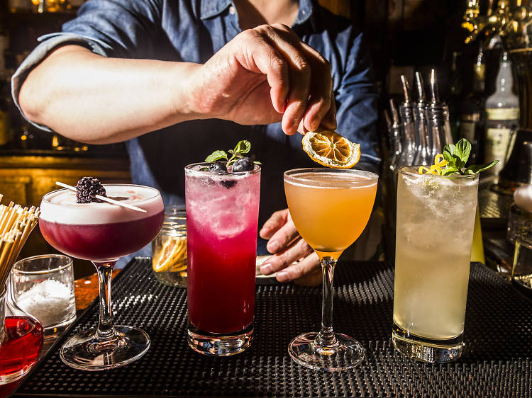 A hand places garnishes on four cocktails at a bar