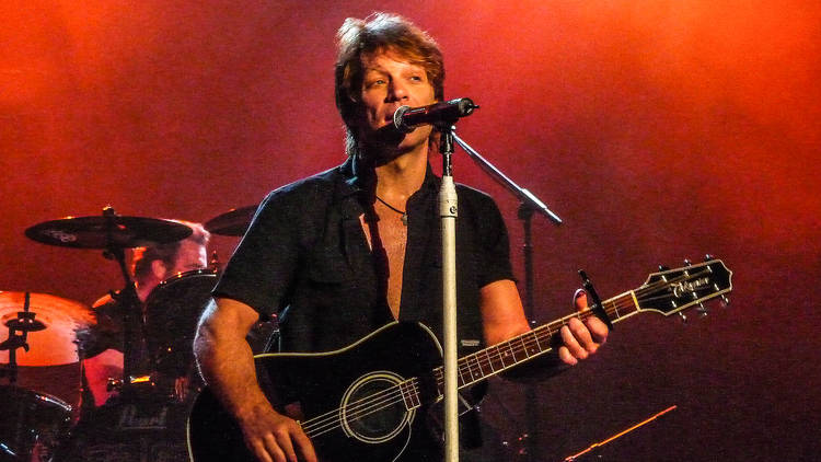 Musician Jon Bon Jovi in concert on stage holding a guitar