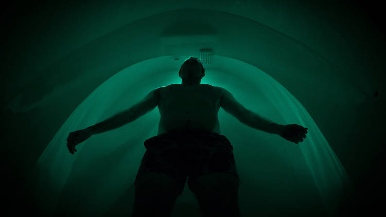 Man floats inside dark pod.