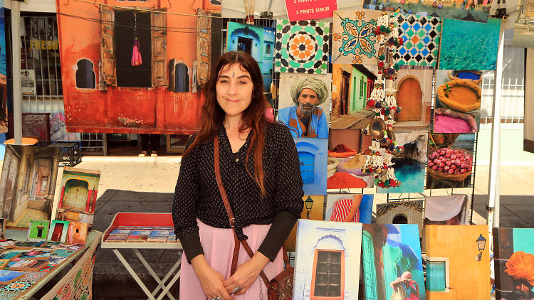 Woman stands in front of a colourful market stall.