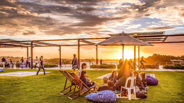 People sit on the grass watching the sunset over water.