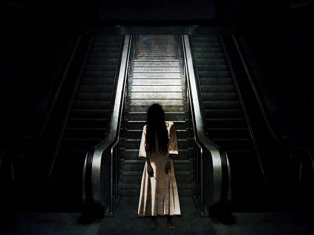 Bloodfest Creepy woman stands in front of escalator.