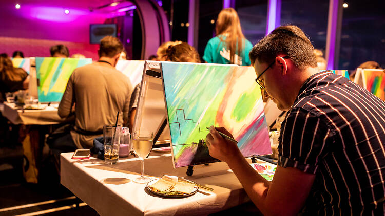 People painting on canvas and drinking wine.
