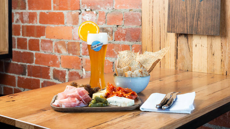 A cheese and cured meats board with a Blue Moon beer