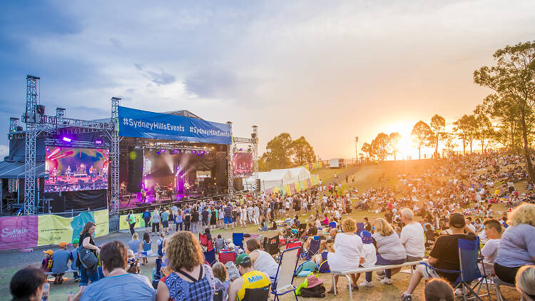 People sitting on a hill at sunset looking at a stage.