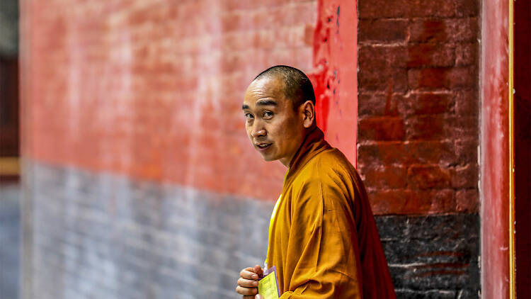 Monk standing near a red wall.