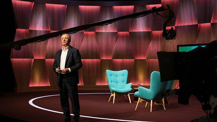 Andrew Denton stands on stage with boom mic.