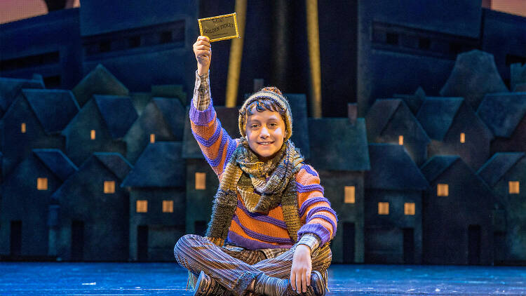 Actor playing Charlie bucket holds golden ticket on stage.