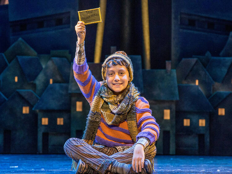 Actor playing Charlie bucket holds golden ticket on stage.