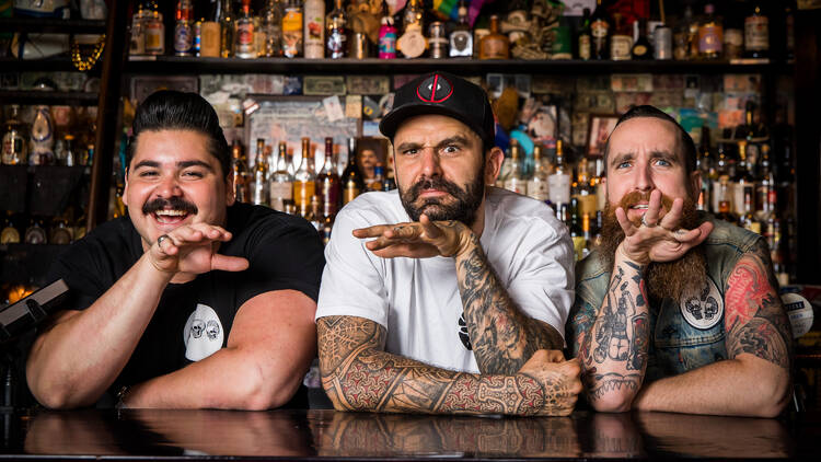 Three people standing behind a bar 