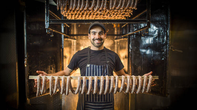 Man holding sausages in front of burning oven