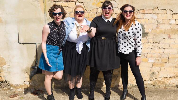 Band members pose together in front of a brick wall.