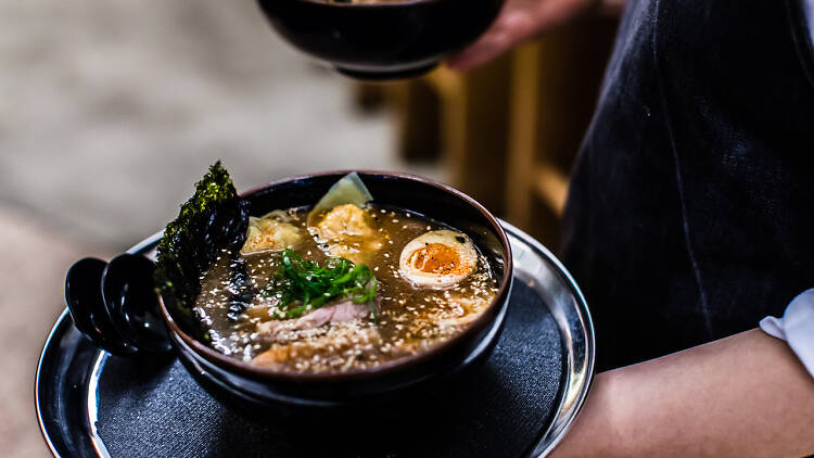 A bowl of ramen being held by waitstaff