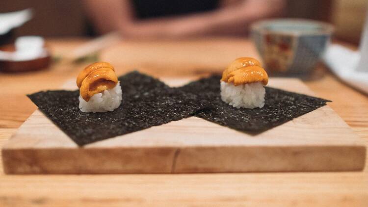 Two pieces of sushi with uni on top of rice on a wooden board