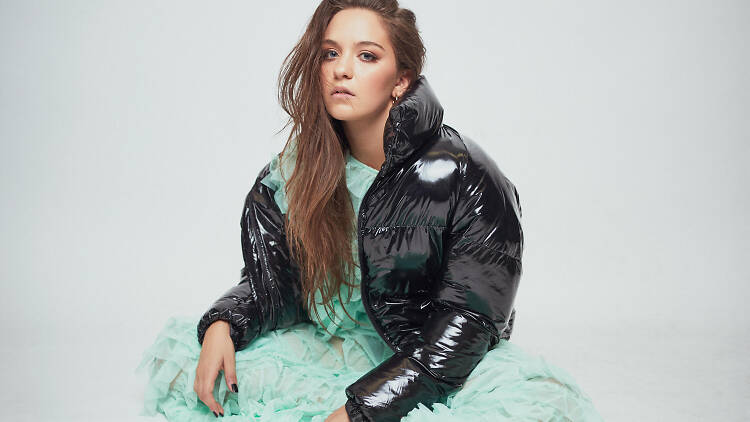 Musician Cxloe in a press photo wearing a green dress and black coat