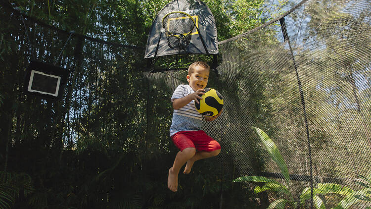 Kid jumping on a trampoline with a ball.