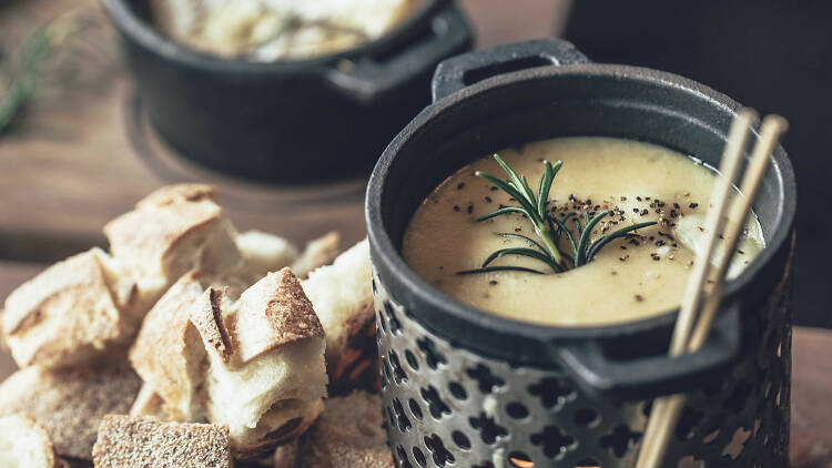 Cheese fondue and cubes of bread on a wooden board
