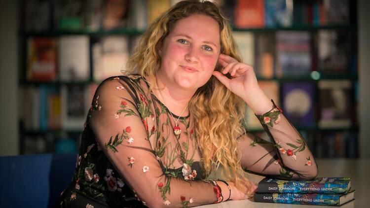 Author Daisy Johnson (Everything Under) learning on the table with books