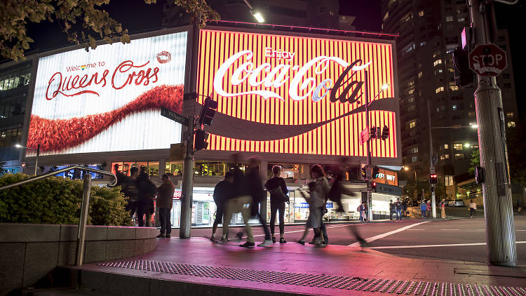 People walking at night in front of the Coke sign at Kings Cross