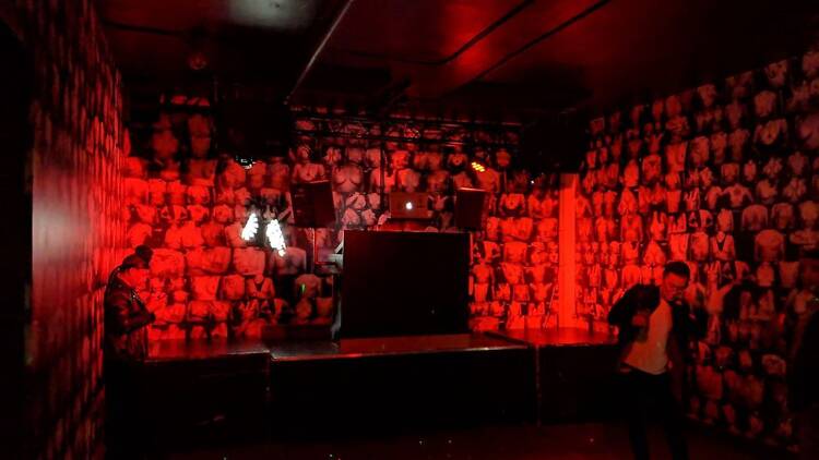 A red lit dance floor with photos of breasts papering the walls