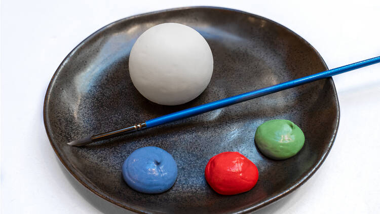 White sphere with blue, red and green dollops of food on a black plate, with a paint brush