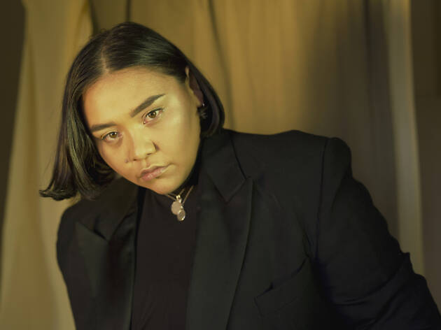 Kira Puru Artist Kira Puru wearing black in front of a yellow curtain.