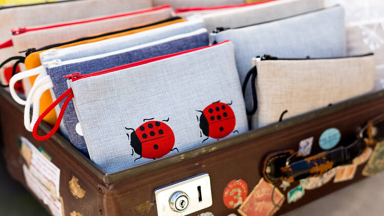 A suitcase with stickers and pins on it full of cute embroidered purses. 