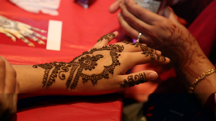 Hands with henna tattoo on a red table.