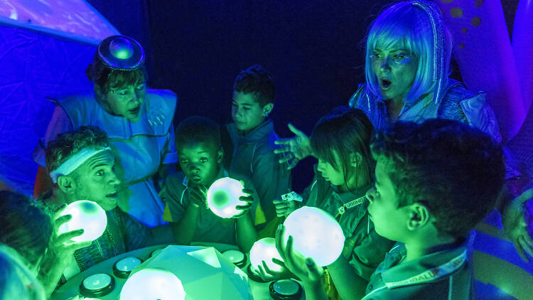 Kids and performers gazing in awe at glowing green orbs