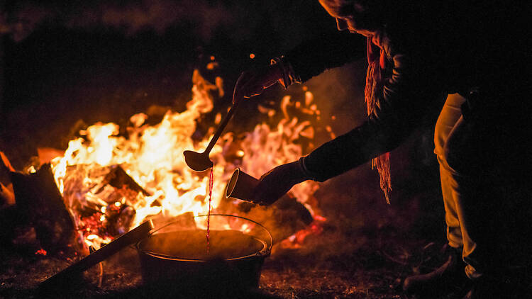 A person pouring a drink in front of a bonfire at the Orange Winter fire Festival.