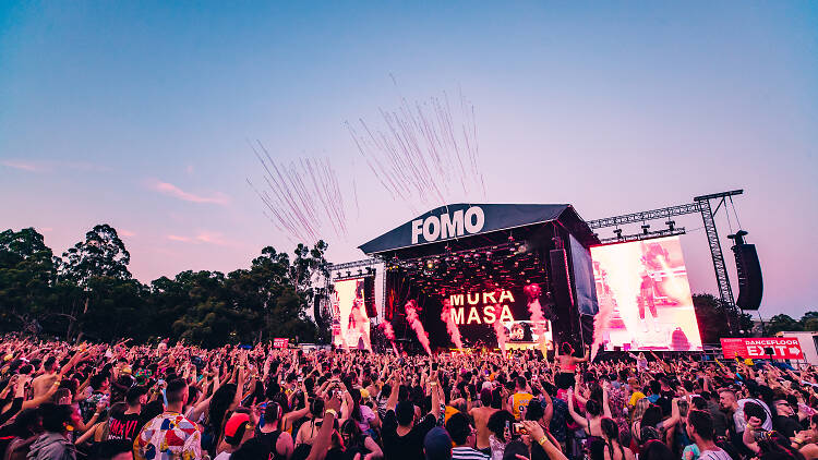 Crowd of people dancing at FOMO Festival as the sun sets.