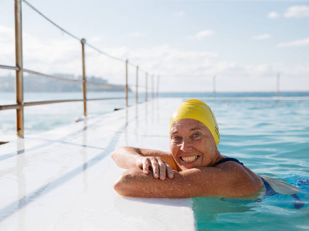 Nicki Vinnicombe, assistant starter at Bondi Icebergs, at the pool Nicki Vinnicombe, a swimmer at Bondi Icebergs, resting her arms on the side of the pool wearing a yellow swim cap