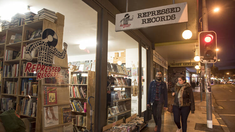 Two people walking outside Repressed Records store in Newtown at night