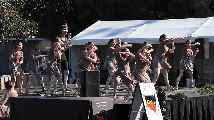 Young Indigenous dancers in traditional dress from Redfern Dance Company dance on stage.