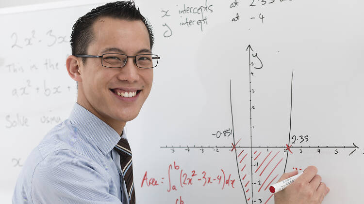 Mathematician Eddie Woo smiling and writing on a white board.