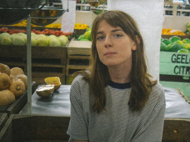 Angie McMahon - 2019 Melbourne artist Angie McMahon sitting outside a fruit shop in a striped t-shirt.
