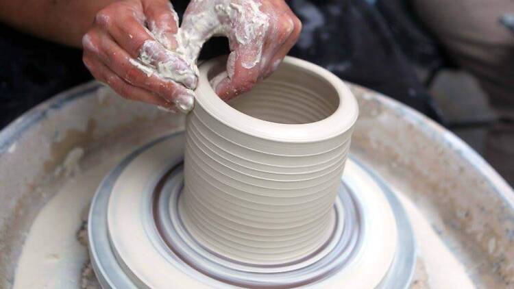 Two hands creating a ceramic vessel on a wheel