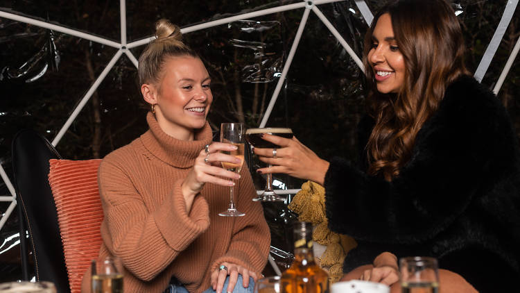 Two women cheersing glasses in a see through igloo