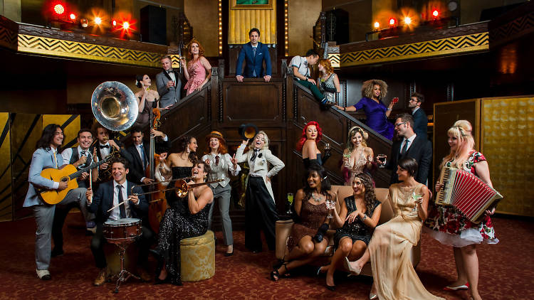 The Postmodern Jukebox crew sitting on stairs with instruments.