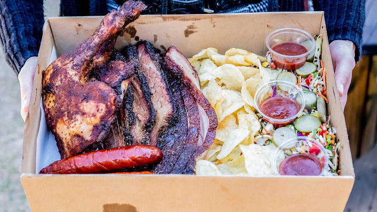 A tray of barbecue meat, chips, salad and sauce.