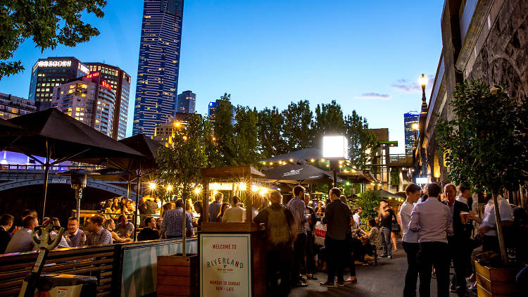 Busy outdoor bar area at twilight, cityscape in background