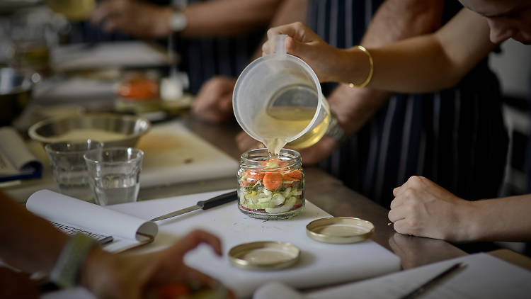 People pouring vinegar into a jar of veggies to make pickles.