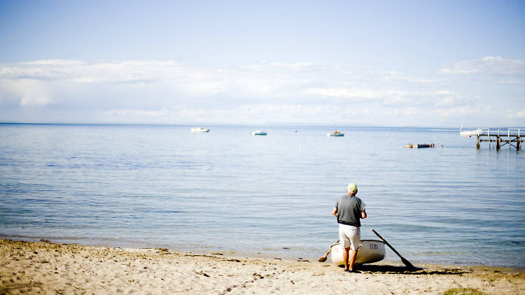 Man standing next to rowboat on the seashore 