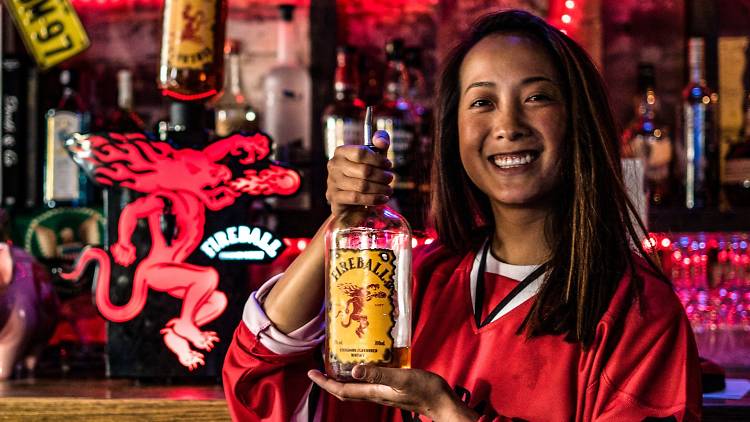 Woman holding a bottle of Fireball Cinnamon Whisky behind a bar.