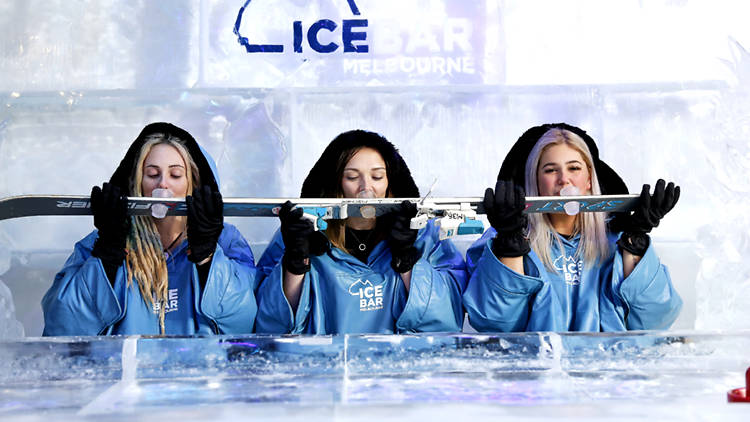 Women in blue coats drinking shots from a ski