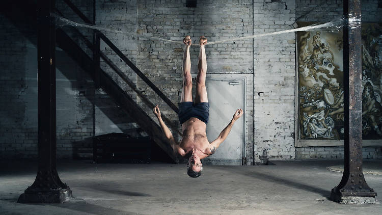 Performer Lee Wilson hanging upside down on tape by his feet