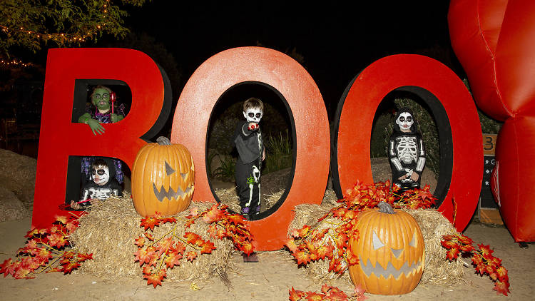 Kids in Halloween costumes posing against a giant 'Boo' sign